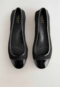 Svarta ballerinas med ett ovandel i mocka och tåhuvud i lackläder. Har en perforerad innersula för komfort och söm längs kanten.