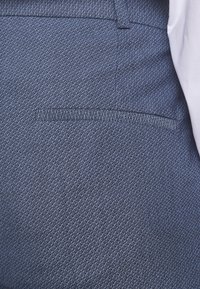 Pantalons bleu sur mesure avec un motif en chevrons texturé ; comprend une poche arrière et une taille lisse, fabriqués à partir d'un tissu durable.