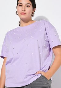 Lavendel kortærmet t-shirt lavet af blødt stof, prydet med hvide dekorative perler arrangeret jævnt over fronten. Casual pasform.