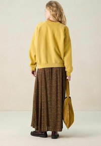 Gele oversized sweatshirt met raglanmouwen, gecombineerd met een bruine maxi rok met luipaardprint. Geaccessoriseerd met een gele schoudertas.