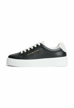 Sort sneaker med lavt skaft med hvid sål og snørebånd, hvid hælkappe og gyldt Tommy Hilfiger-logo på siden.