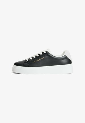 Basket basse noire avec semelle et lacets blancs, languette de talon blanche et logo Tommy Hilfiger doré sur le côté.
