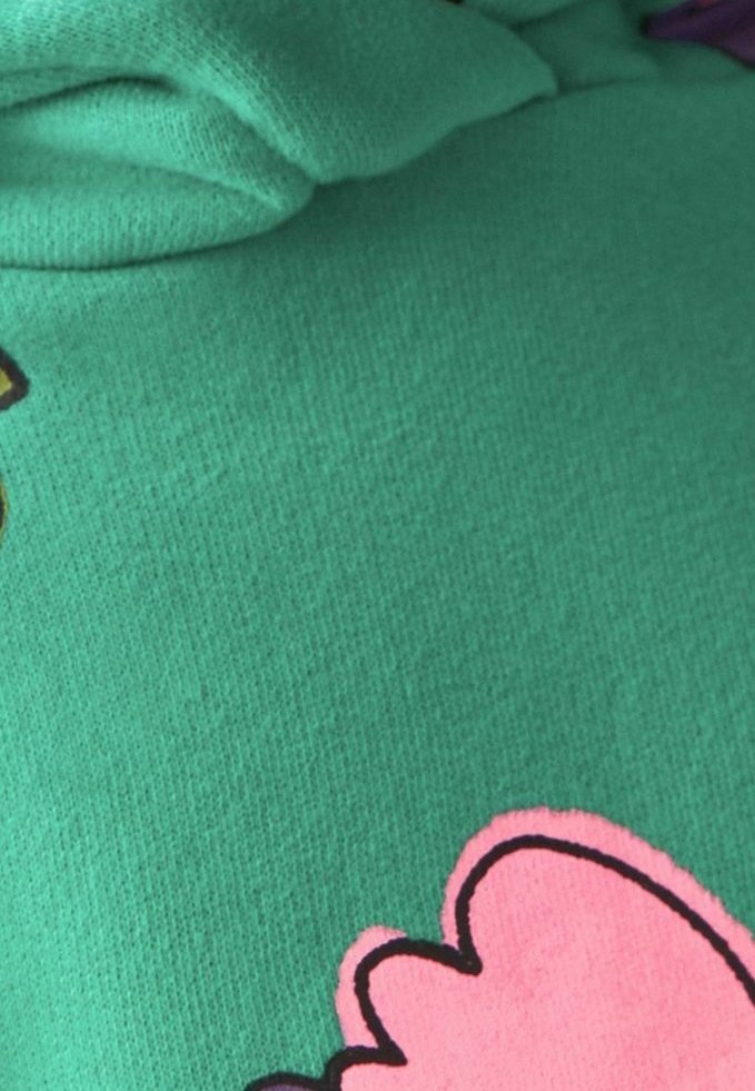 Tissu vert avec un grand contour de fleur rose et couture texturée pliée, montrant une partie d'un motif textile.