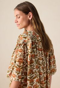 Blumenbluse aus leichtem Stoff mit orangefarbenen und grünen Mustern, kurzen Puffärmeln und einem gerafften Ausschnitt. Natürlicher, weicher Griff.