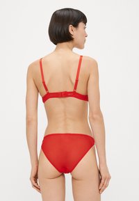 Rdeče spodnje perilo iz prosojnega materiala z nastavljivimi naramnicami in valovitim robom na hlačkah, s gladkim dizajnom.