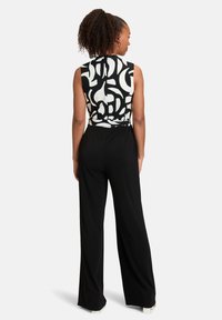 Zwarte wijde jumpsuit met een mouwloze top in een abstract zwart-wit patroon. Glad materiaal met een strik in de taille.