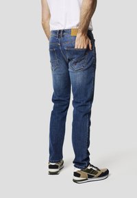 Blå denimjeans med en lige pasform, synlige sømme og to baglommer. Båret med sorte og beige træningssko.
