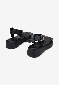 Black platform sandals with a sleek design, made of smooth leather, featuring adjustable crossover straps and a gold-tone buckle accent.