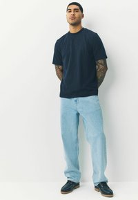Marineblå ribbet t-shirt med korte ærmer kombineret med lyseblå løstsiddende jeans og mørke sko, med syninger og et afslappet design.