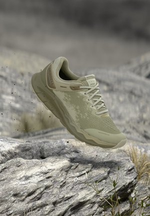 Chaussure de randonnée imperméable Merrell vert clair en l'air au-dessus d'un terrain rocheux avec de petites plantes et un arrière-plan flou.