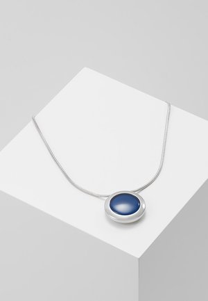 Collier en argent avec un pendentif en pierre précieuse bleue lisse et ronde reposant sur une surface géométrique blanche.