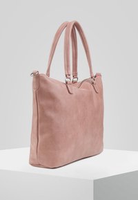 Różowa torebka typu tote z zamszu z dwoma uchwytami, o prostokątnym kształcie, gładkiej fakturze i górnym zamkiem błyskawicznym, na szarym tle.