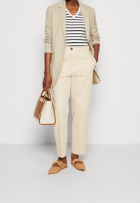 Blazer beige, camiseta de rayas blancas y azul marino con cuello en V, pantalones beige claro, zapatos tipo sandalia en tono tan y un bolso pequeño bicolor.