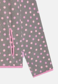 Grauer Fleece-Stoff mit großen rosa und hellrosa Punkten, ausgestattet mit einem rosa Rand und einer Seitentasche. Weicher Stoff, lässiges Design.