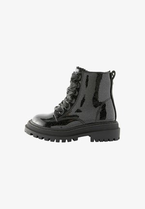 Botte de combat noire brillante avec semelle épaisse à crampons et lacets en ruban de satin, vue de côté sur fond blanc.