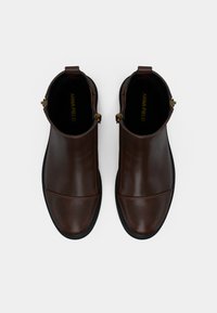 Botas castanhas de couro até ao tornozelo com textura lisa, apresentando biqueira arredondada, sola preta e detalhes em dourado na parte superior.