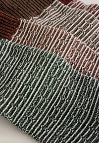 Adīta auduma audums ar svītrām brūnā, krēmkrāsas un zaļā krāsā, ar dažādām tekstūrām un līnijām. Mīkstās, daudzkrāsainās pavedienos veido slāņveida izskatu.