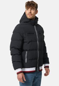 Black puffer jacket with a zippered front, two zippered chest pockets, elastic cuffs, and red and white ribbed hem. Features a hood.