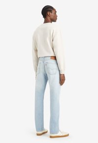 Light blue straight-leg jeans with a faded finish, brown leather patch, and white sneakers worn with a beige sweatshirt.