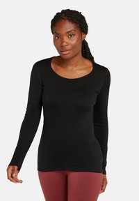 Top negro de manga larga hecho de una tela suave con escote redondo y diseño ajustado, combinado con leggings color burdeos. Textura lisa y líneas limpias.