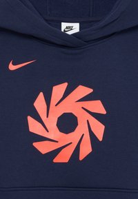 Tmavomodrá mikina Nike s kapucňou so červeným vírivým geometrickým vzorom, umiestneným pod malým červeným logom Nike swoosh.