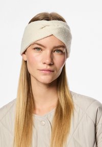 Fascia per capelli color crema lavorata a maglia con un design a torsione, realizzata in tessuto morbido, indossata da una modella con capelli biondi lisci.