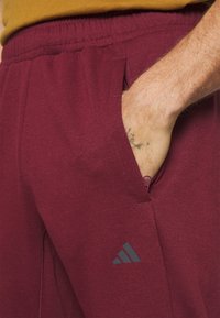 Bordeaux sportbroek met een zijzak, elastische tailleband en een grijs Adidas-logo. Zachte, gestructureerde stof en een strak design.