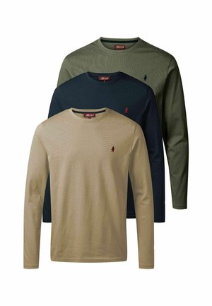 Mężczyzna z brodą i wytatuowaną ręką, ubraną zieloną koszulę z długim rękawem, brązowe spodnie i czarne buty, stojący na białym tle.