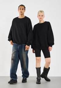 Felpe oversize nere indossate da due modelli, abbinate a denim strappato e shorts neri a coste. Stivali neri testurizzati con dettagli in metallo.