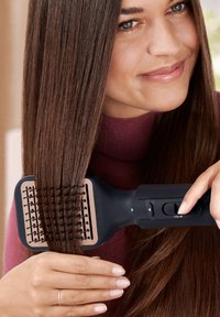 Fer à lisser électrique avec un corps noir, une large paddle et une surface de chauffe texturée, coiffant des cheveux longs et lisses.