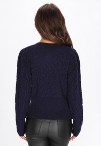 Merihenkinen neulepaita, jossa on teksturoitu, neulottu kangas ja puffimaiset hihat; ribattu helma; yhdistetty mustiin tekonahkahousuihin.