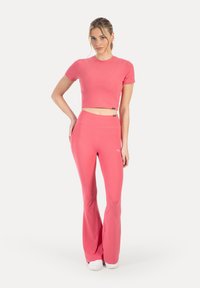 Rosa kort topp och utsvängda byxor i stretchigt material med slät yta och figursydd design. Skorna är vita och vardagliga.