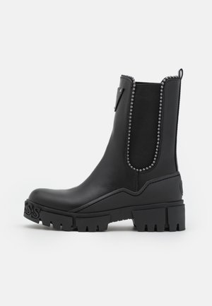 Czarne botki za kostkę wykonane z gładkiej skóry, wyposażone w elastyczne boczne panele, ozdobione nitami, z grubą gumową podeszwą i podwyższonym obcasem.