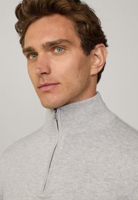 Grau gefütterter Pullover mit hohem Kragen. Weicher, strukturiertes Material. Subtiles Muster, taillierte Passform, mit eingelassenem Reißverschluss auf der Vorderseite.