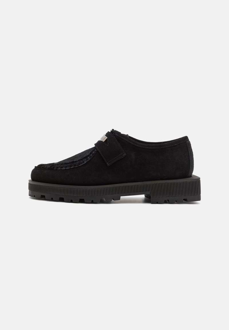 Chaussure en daim noir avec des accents texturés, une semelle plate et une fermeture à l'aide d'une sangle. Dispose d'une semelle en caoutchouc épaisse et rainurée, ainsi que de lignes épurées.