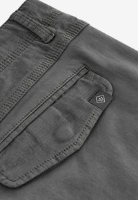 Grauer Stoff mit einer Tasche, die ein schwarz etikett hat. Das Material wirkt strukturiert, mit sichtbaren Nähten entlang der Kanten.