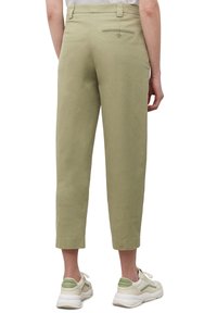Personne portant un pantalon court vert olive clair avec une poche arrière boutonnée et des baskets blanches avec des accents verts, vue de dos.