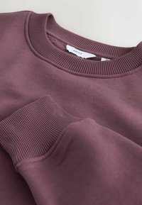 Bordó pulóver bordázott nyakkal és mandzsettával, puha textúrával és finom varrási részlettel. A márkajelzés belül látható.