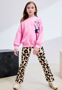 Rosa sweatshirt med blomsterprint på venstre side; kombineret med beige udvidede leggings med sort leopardmønster; hvide sneakers med brune accenter.
