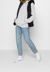 Szara bluza z kapturem i troczkami, czarna kamizelka z sztucznego futra, jasnoniebieskie proste dżinsy oraz białe wysokie trampki z czerwonymi akcentami.