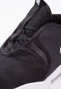 Svart atletiska sneakers med ovandel av mesh, släta textilaccent och vit sula. Inkluderar platta snören och logodetalj på tungan.