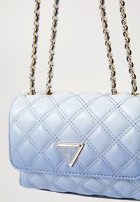 Borsa a tracolla in ecopelle trapuntata di colore azzurro chiaro, con un logo triangolare in argento, cinturini in catena dorata e forma rettangolare compatta.