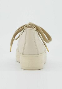 Béžové kožené tenisky s zaoblenou špičkou, strukturovaným svrškem, plochými tkaničkami a zlatými akcenty na koncích; gumová podrážka s embosovanou značkou.