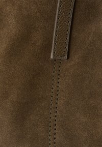 Smeđi nubuk materijal s glatkom teksturom. Sadrži kožne detalje i kontrastnu šav. Dizajn naglašava meku, bogatu boju.