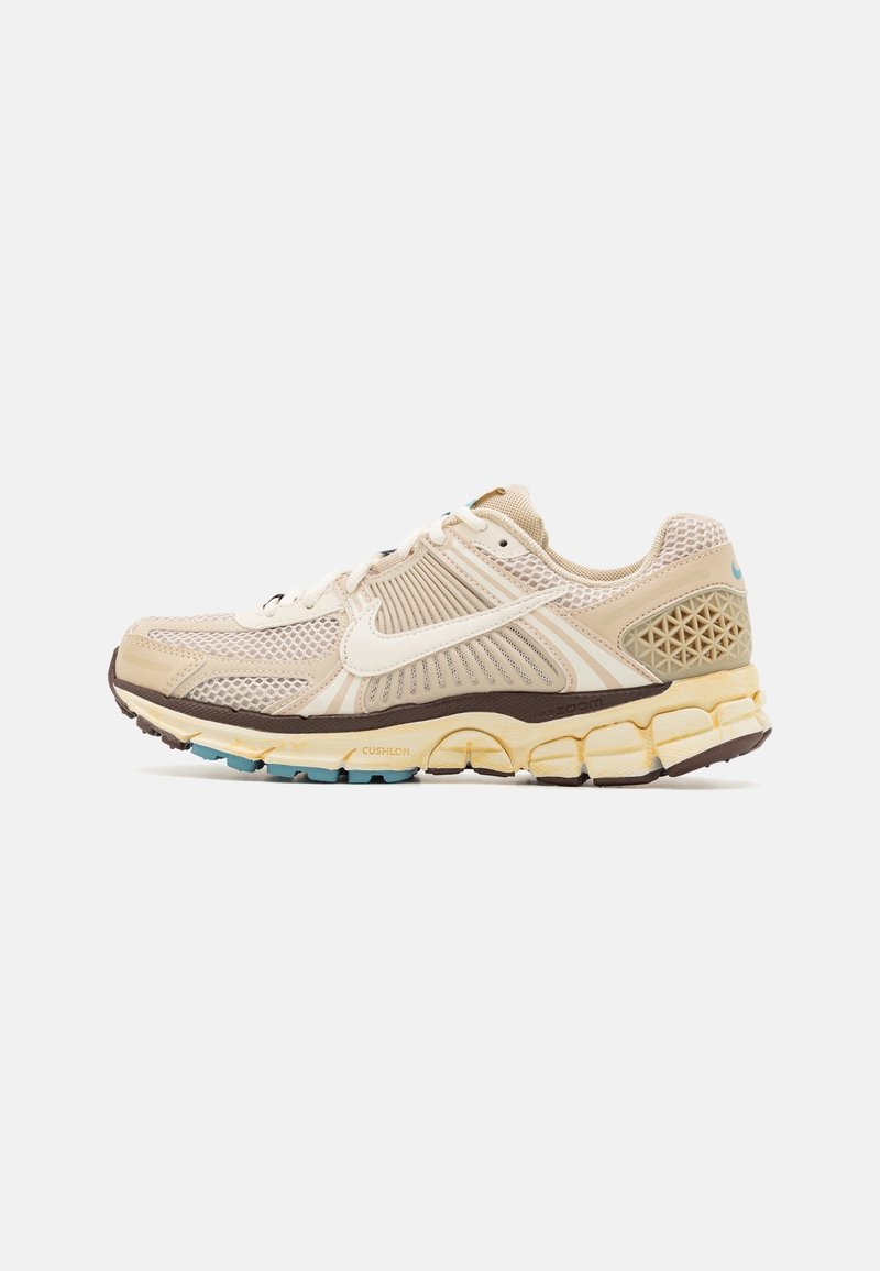 Baskets de sport beiges et crème avec le swoosh blanc de Nike, dessus en maille et synthétique, semelle rembourrée et accents teal sur la semelle extérieure.