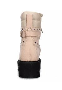 Stivale ankle beige pallido con finitura texturizzata, chiusura con zip, cinturino regolabile e borchie argentate. Suola nera spessa con cuciture dettagliate.