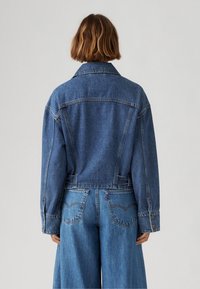 Denim takki, keskikokoinen sininen pesu, ylisuurta istuvuutta, suora leikkaus, terävä kaulus, napilliset hihat, näkyvät tikkausompeleet, yhdistettyinä denim-housujen kanssa.