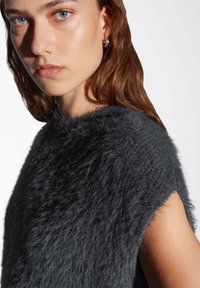 Pull en tricot flou gris foncé avec un col haut et des manches courtes. Présente une finition texturée et une coupe ample. Tissu doux et lisse.