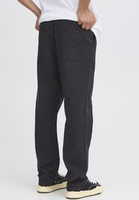 Black cotton pants with a relaxed fit, featuring two back pockets, a smooth texture, and paired with black and cream sneakers.
