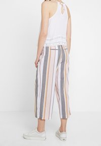 Haut blanc sans manches avec bordure en dentelle et nœud dans le dos, associé à un pantalon à jambes larges rayé multicolore. Tissu léger et coupe décontractée.